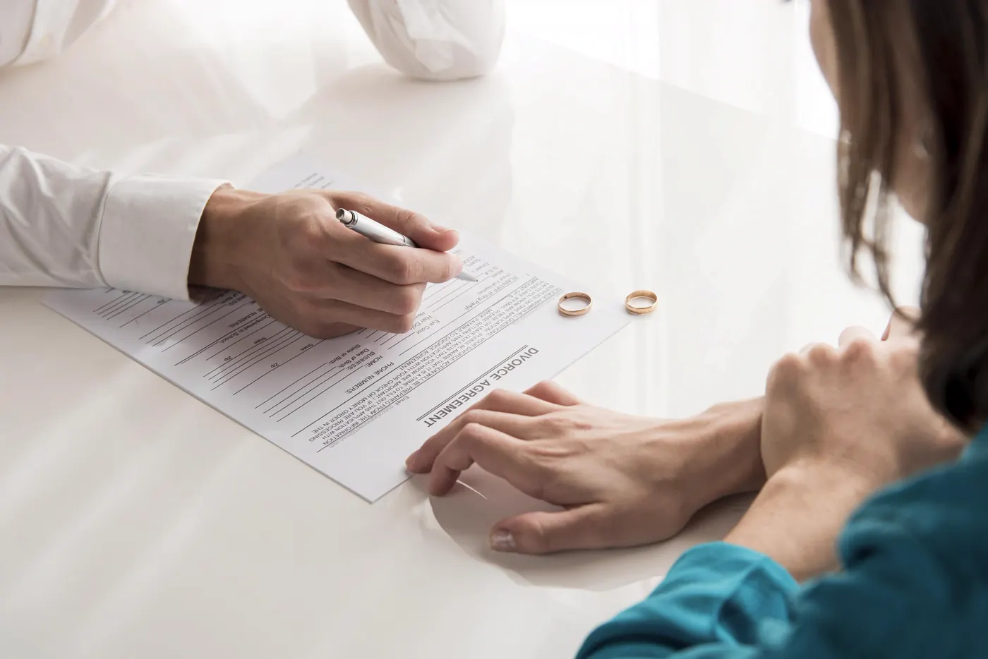 A person signing divorce papers with wedding rings on the table